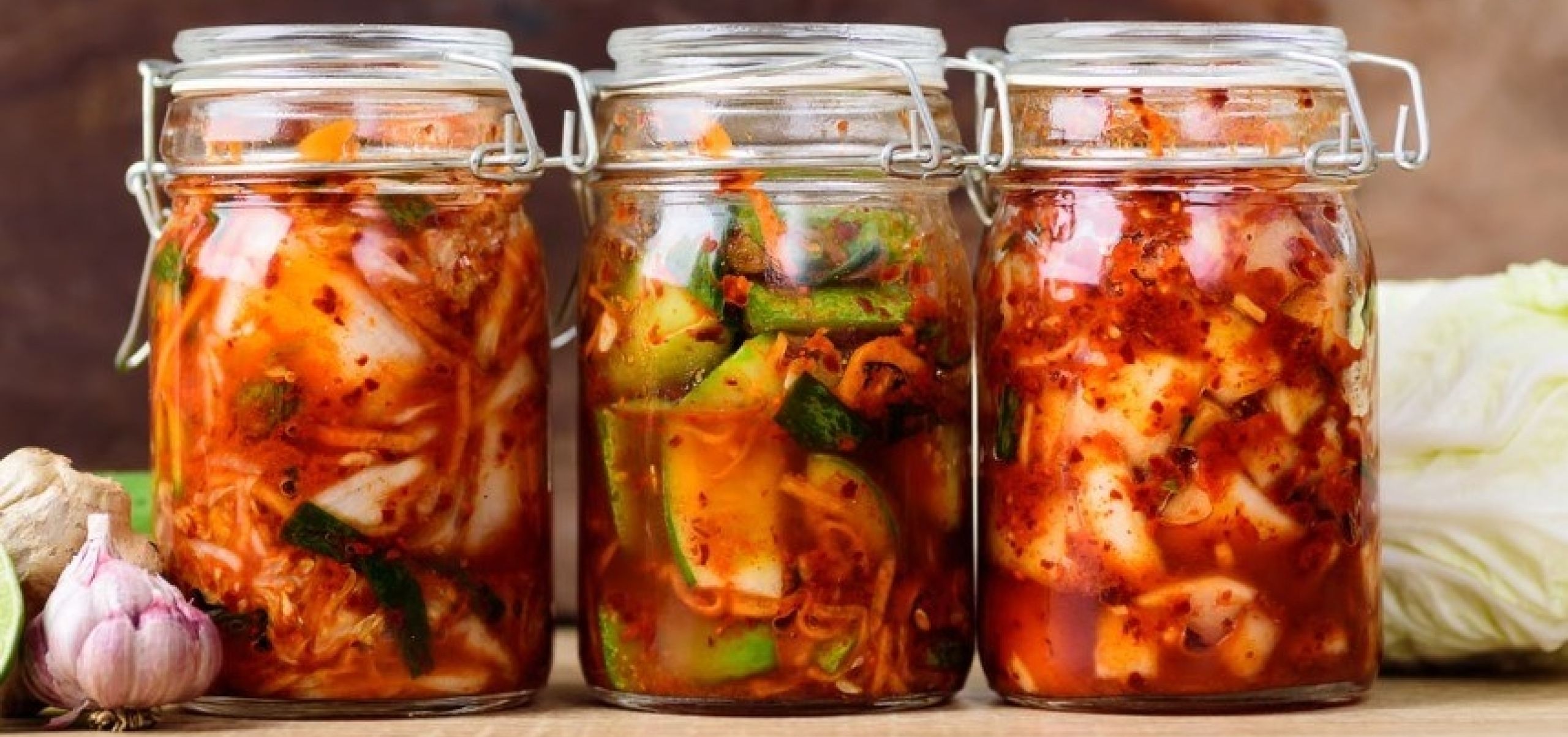 three jars of kimchi lined up on a bench