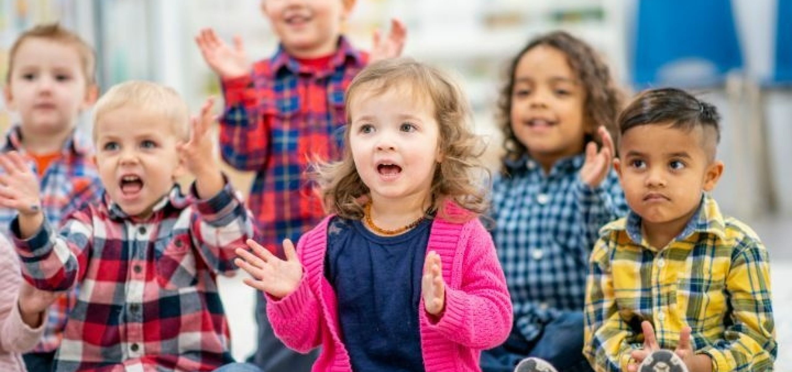 Group of six toddlers sitting on the floor singing sings with hand actions