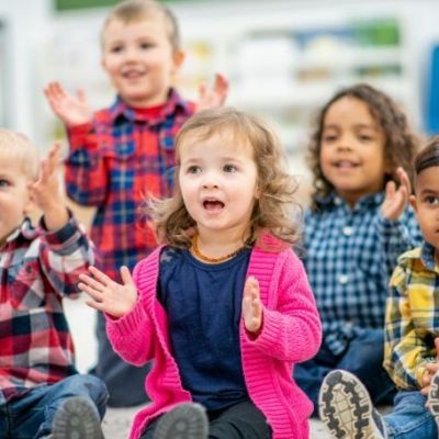 Group of six toddlers sitting on the floor singing sings with hand actions