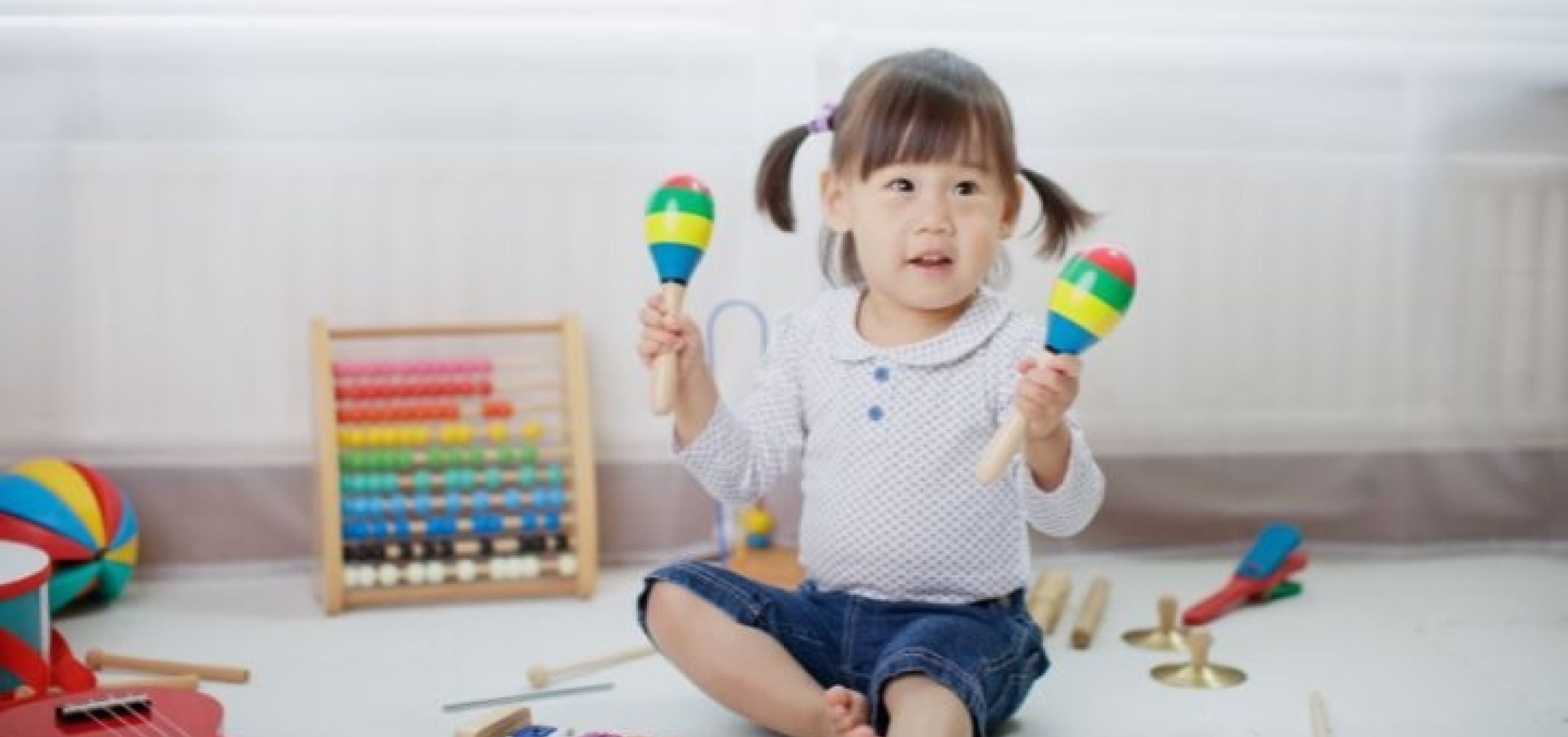 a baby holding 2 maracas sitting on the floor in a playroom