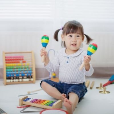 a baby holding 2 maracas sitting on the floor in a playroom