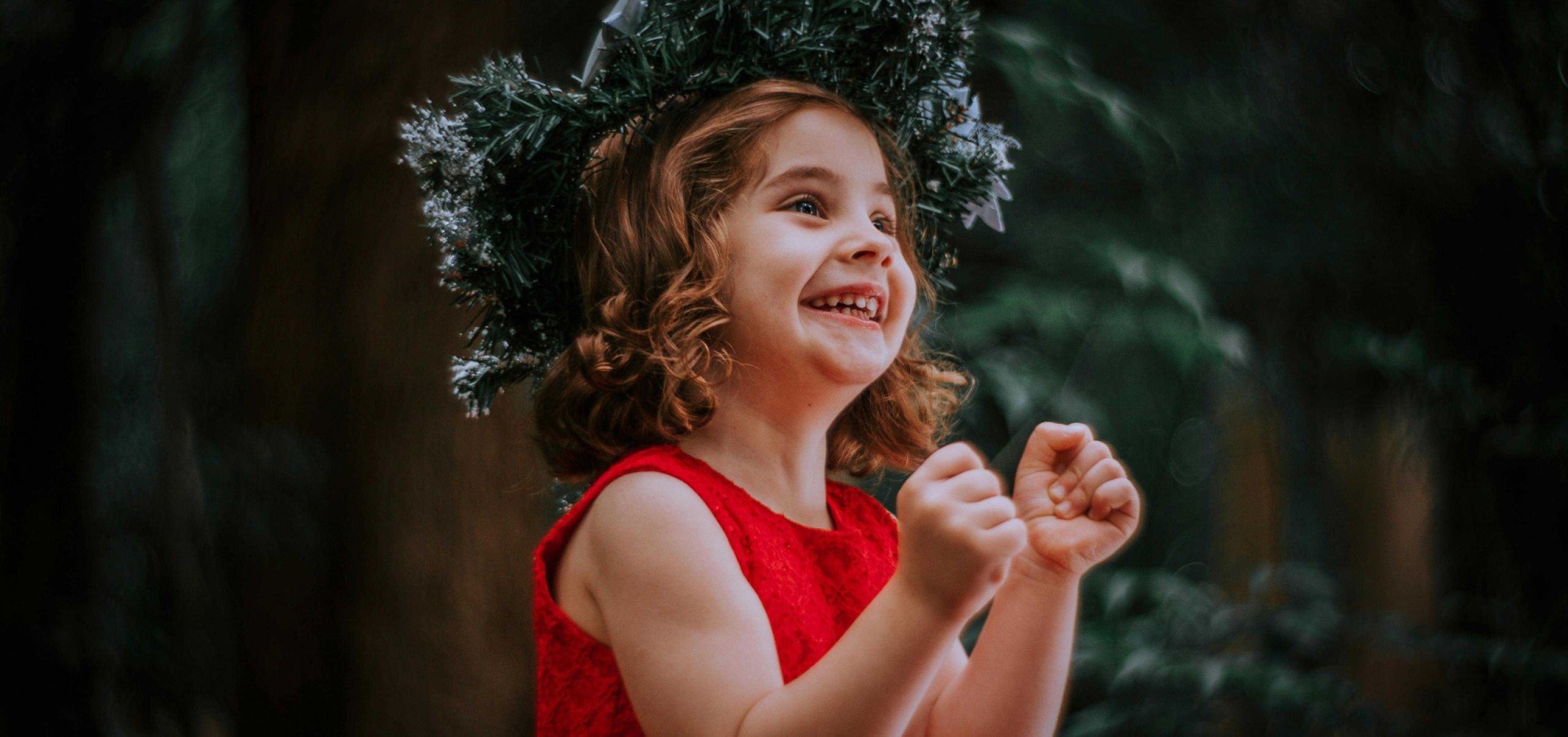 Young girl in a red dress looking excited with a Christmas decorated hat