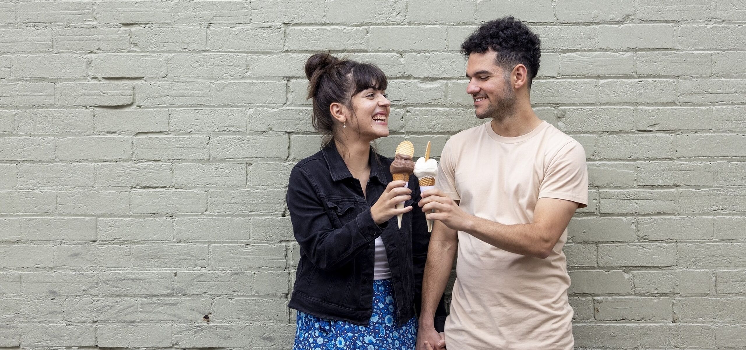 Young woman and man eating ice cream against a white brick wall