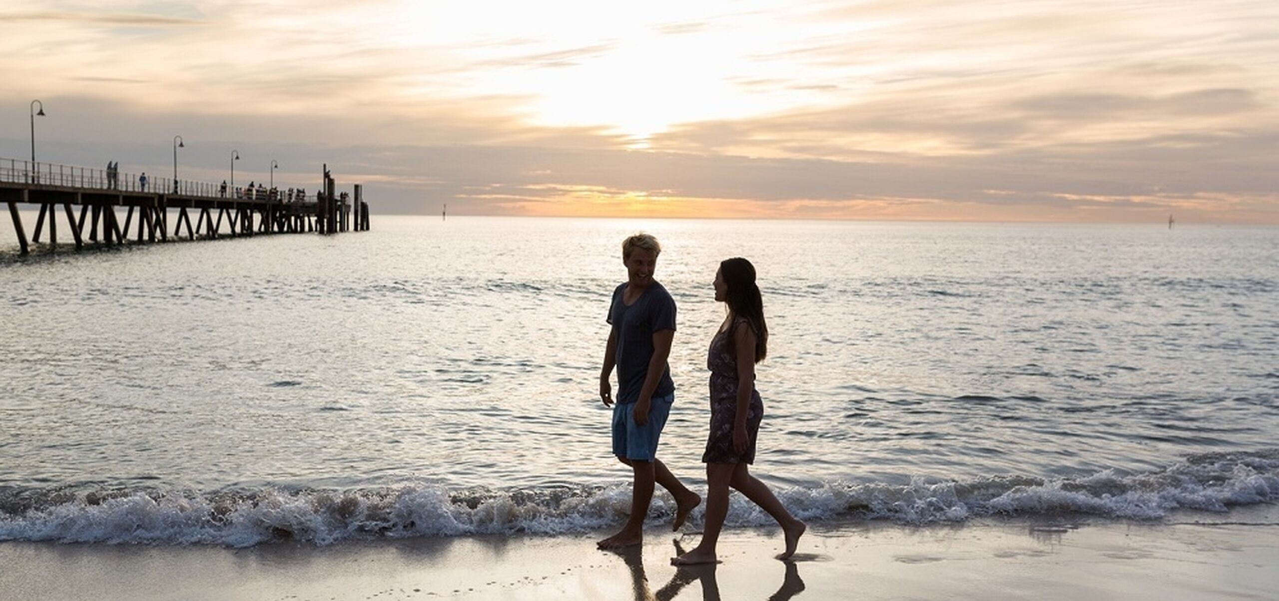 two people walking on glenelg beach at twilight
