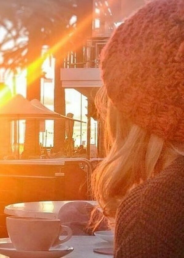lady sitting with back to camera with a cup and saucer on table with winter sun