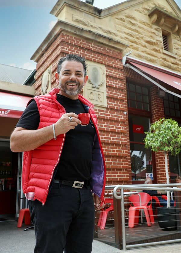 Man holding red espresso cup wearing a red puffer vest, in front of the cibo glenelg building