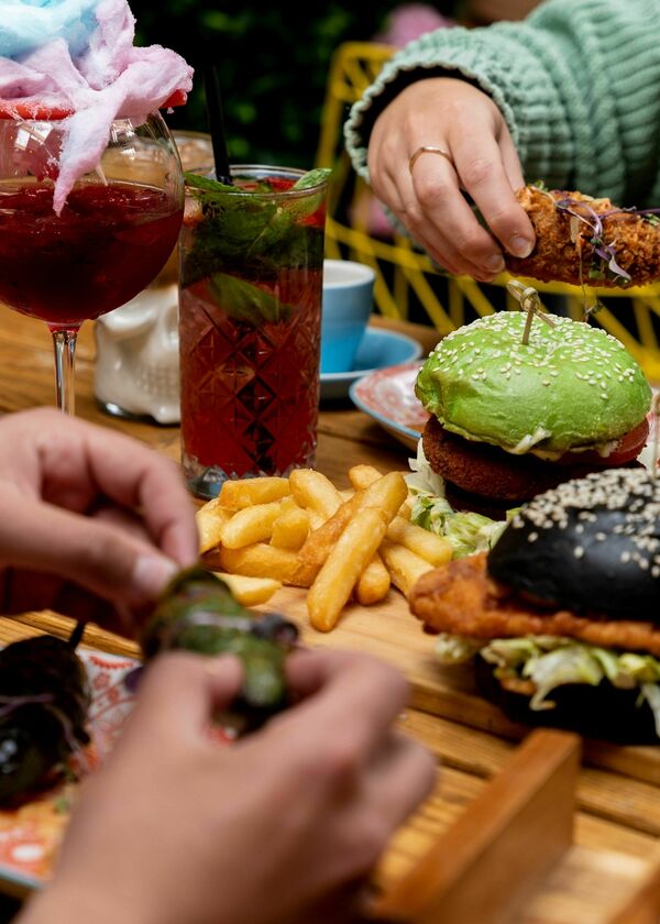 Hands eating burgers and fries with cocktails