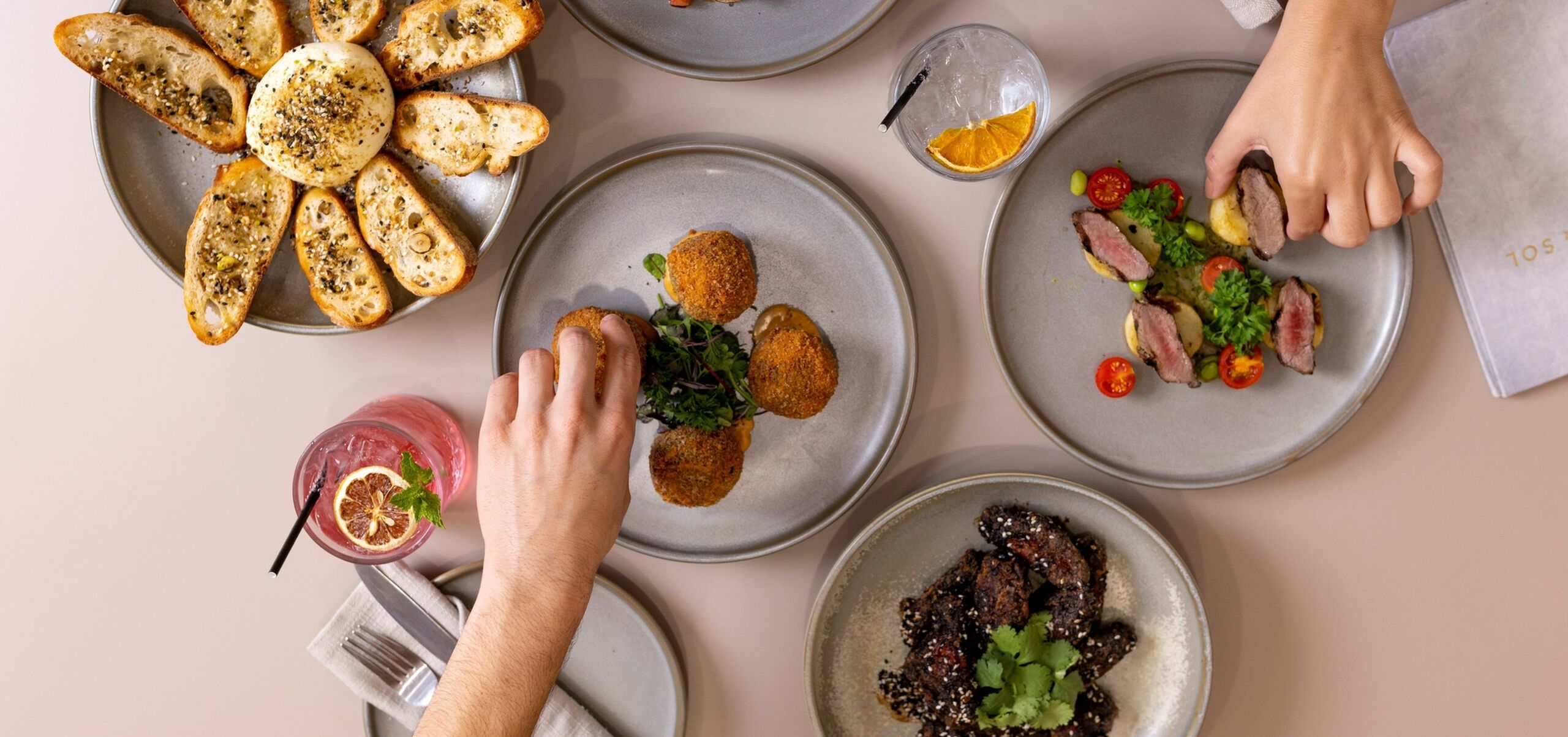 5 plates with small sharing food, with two arms reaching to pick up the food