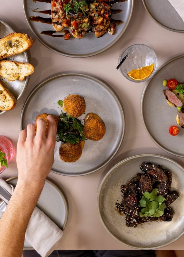 5 plates with small sharing food, with two arms reaching to pick up the food