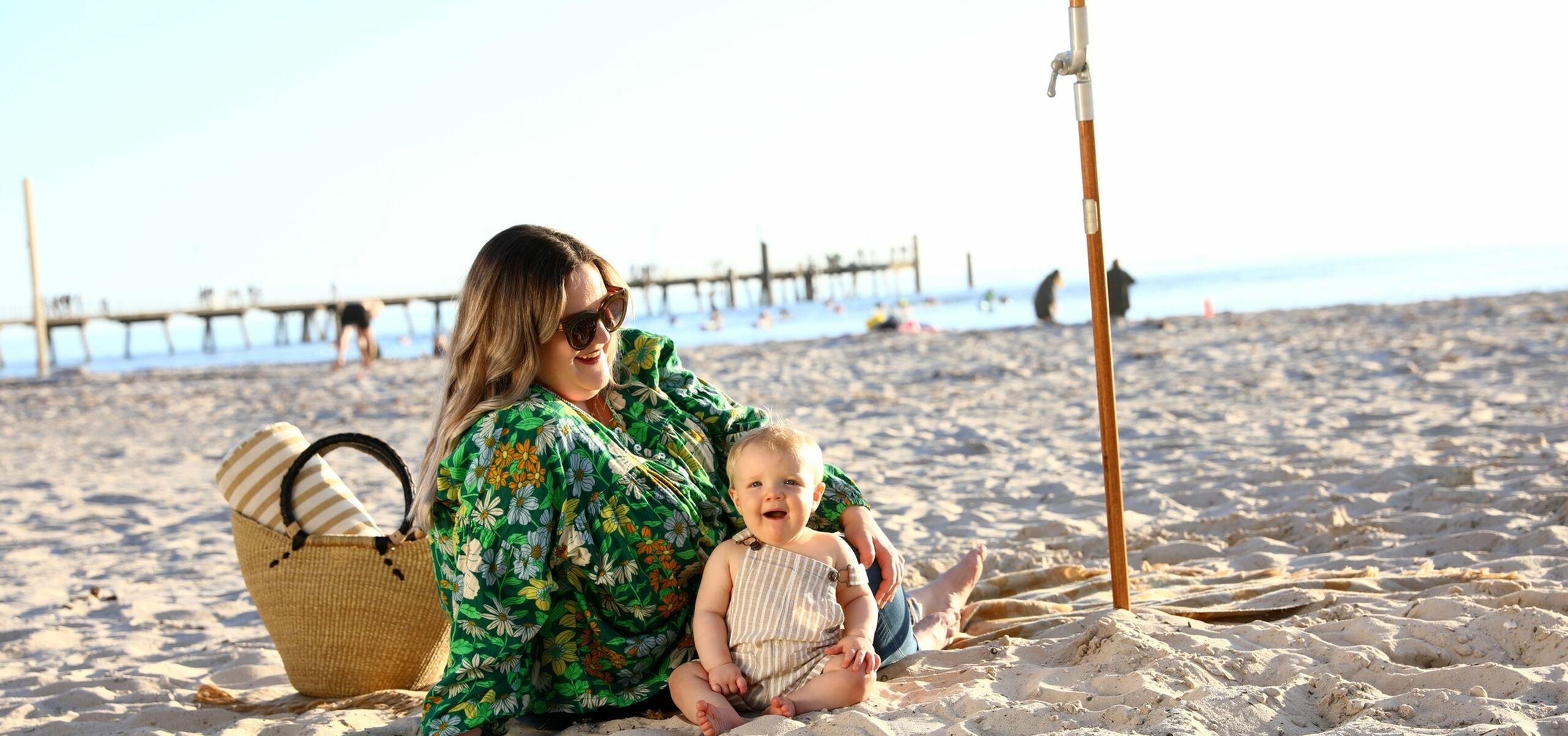 Woman in green top, smiling and sitting with her baby on the beach