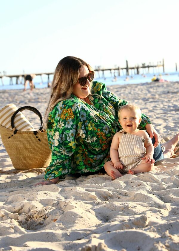 Woman in green top, smiling and sitting with her baby on the beach