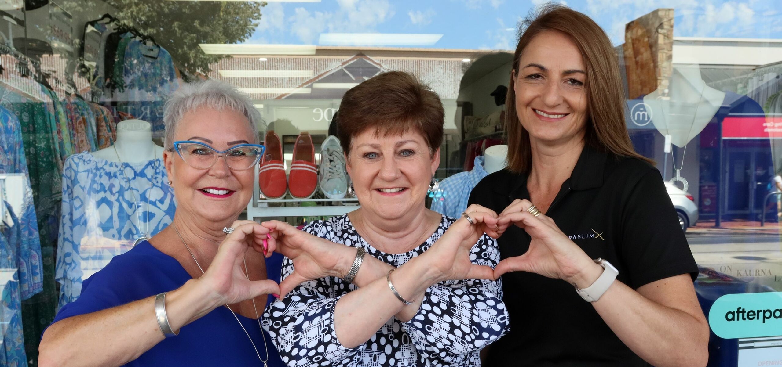 Three women interlocking their hands to make heart symbols.