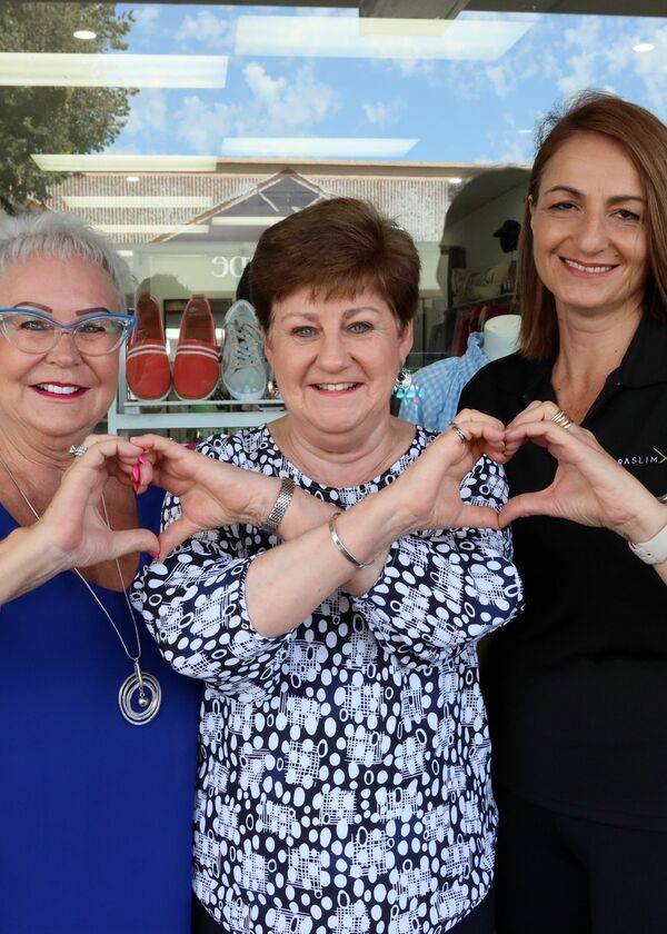 Three women interlocking their hands to make heart symbols.