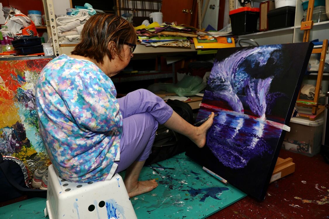 Person in purple pants painting with their feet