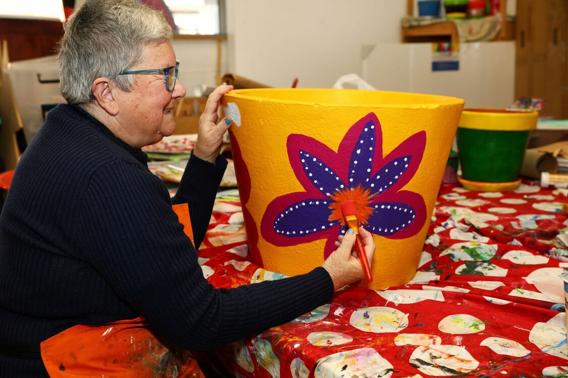 Person painting a flower on a yellow pot
