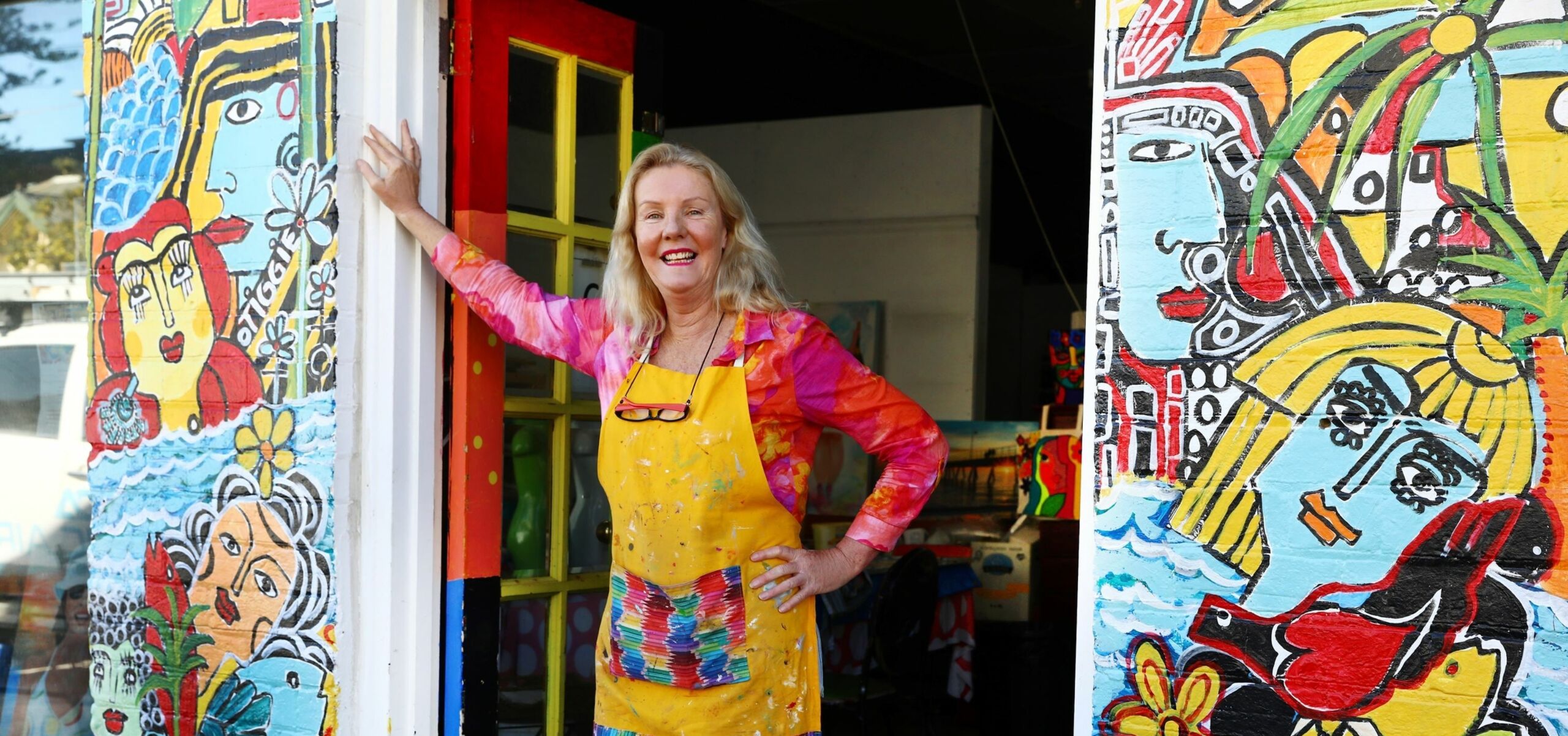 Person smiling in a yellow apron on a colorfully painted wall