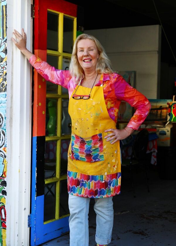 Person smiling in a yellow apron on a colorfully painted wall