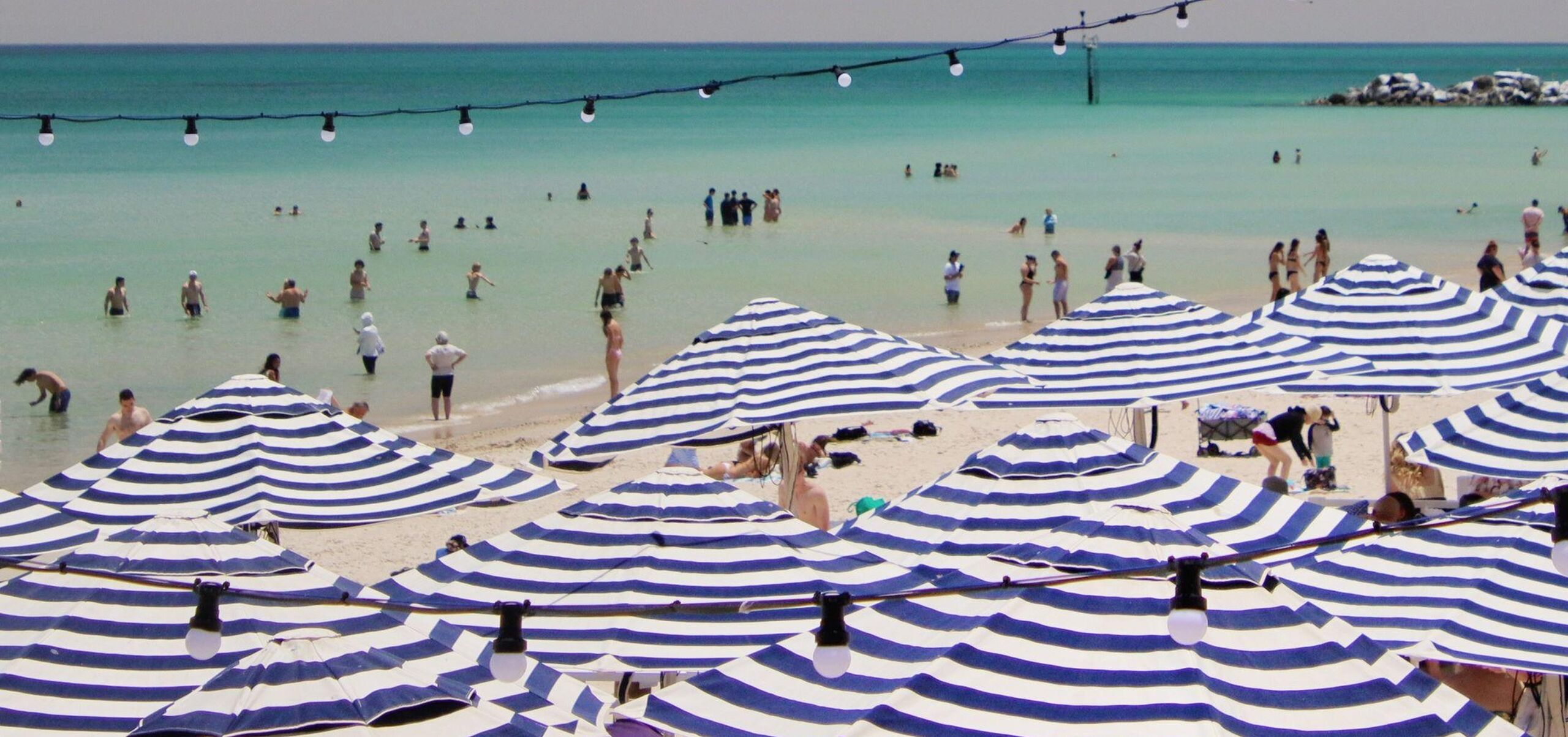 Blue and white umbrellas on the beach with people swimming